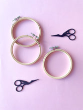 Load image into Gallery viewer, Black and silver stork embroidery scissors, and bamboo embroidery hoops on pink background
